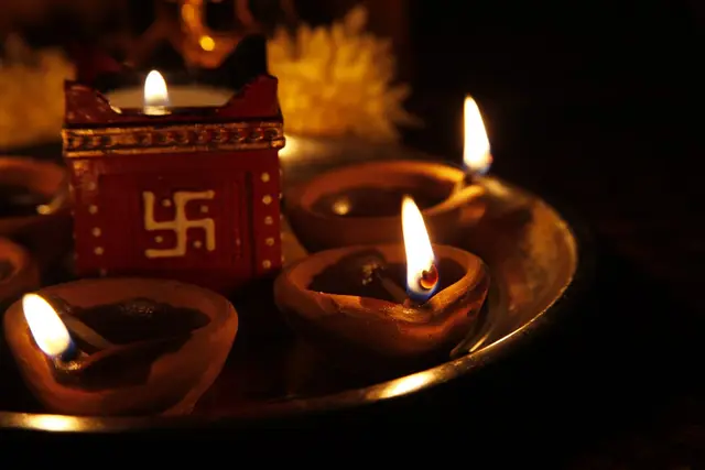 Lit clay diyas and a swastik lamp on a brass thali at Diwali