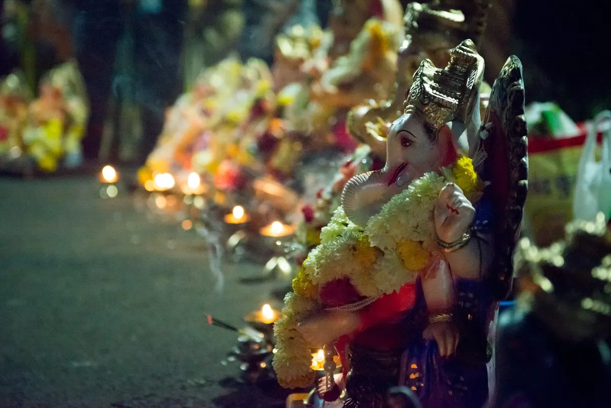 Garlanded Ganesha idol surrounded by oil lamps during Ganesh Chaturthi at night