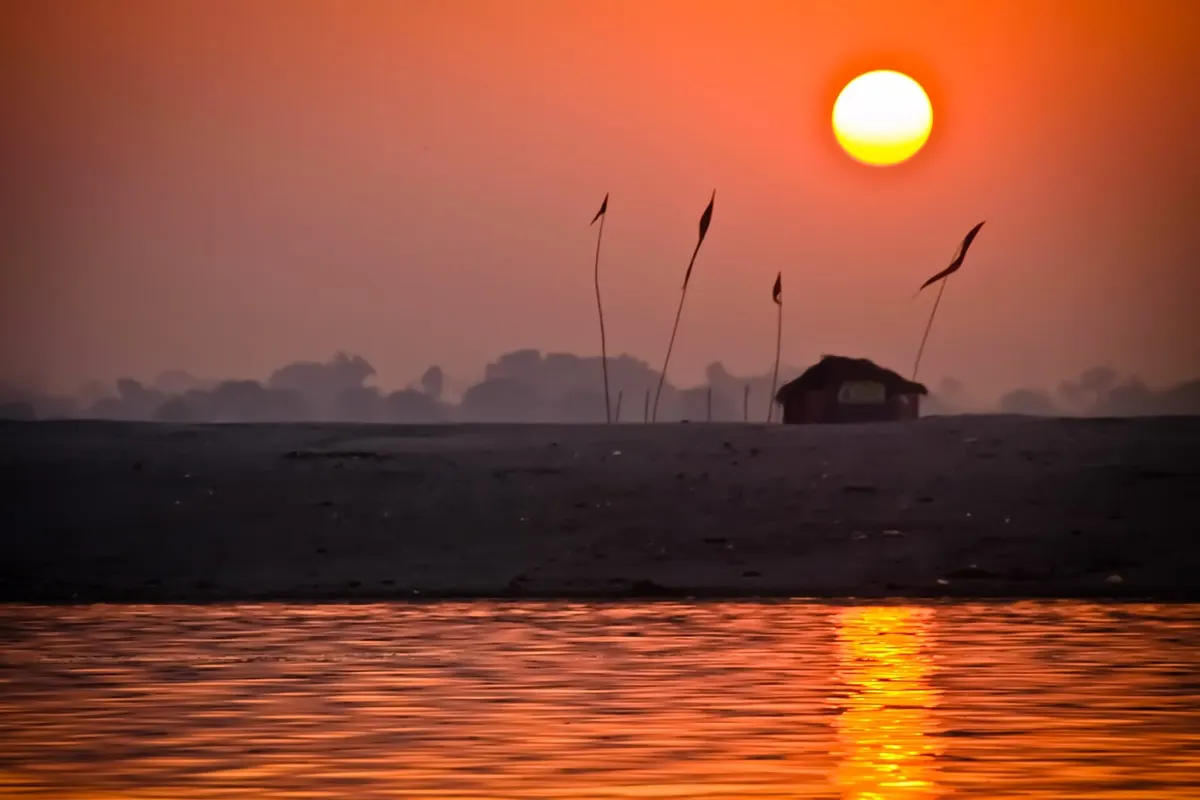 Orange sunrise over the Ganga with flags silhouetted on the far bank