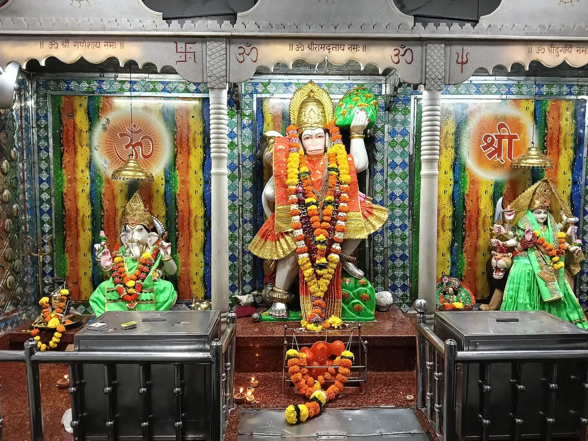 Garlanded Hanuman murti flanked by Ganesha and Durga in a temple darbar