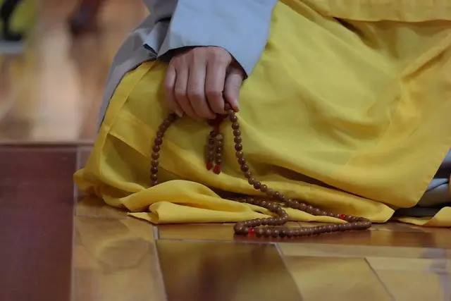 Hand counting wooden japa mala beads while seated in saffron robes