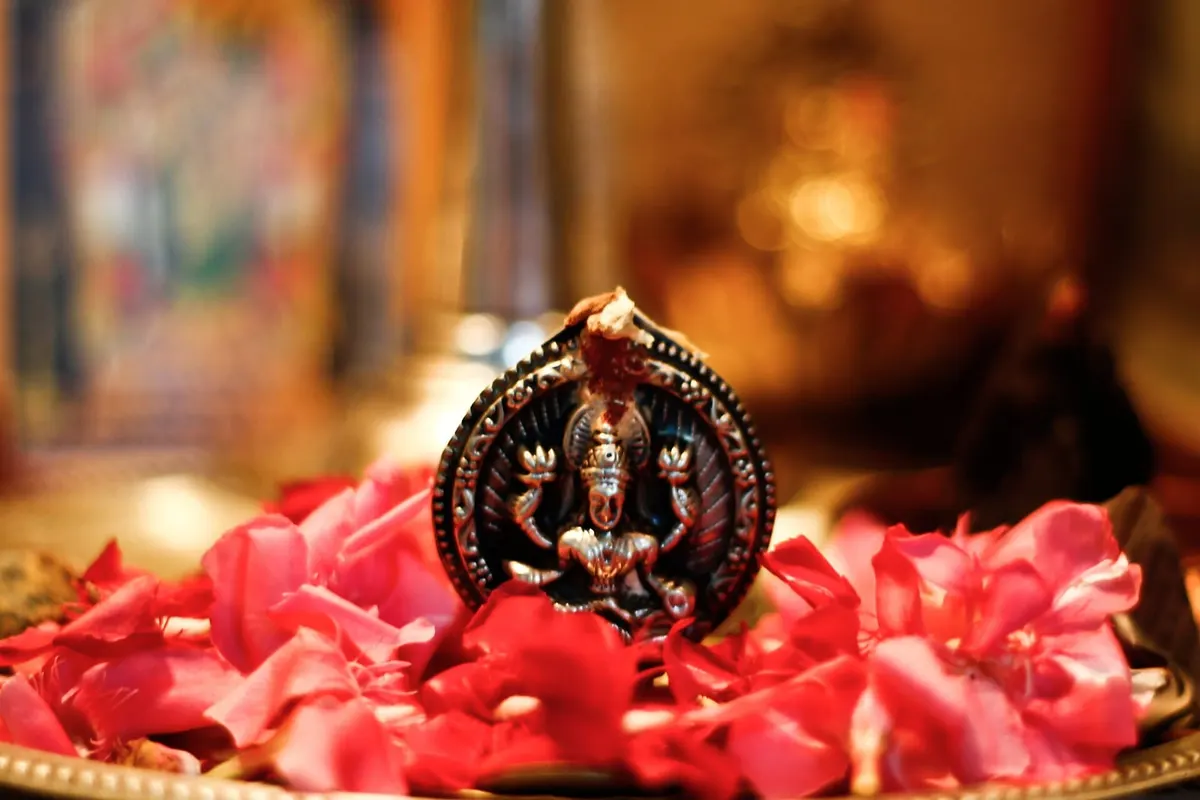 Small Lakshmi murti resting among rose petals in a home temple