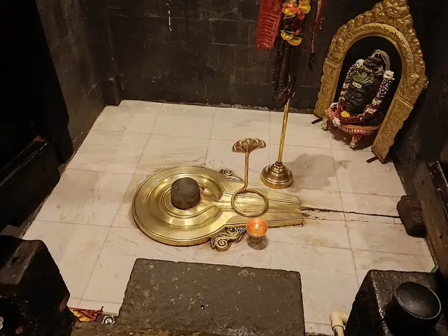 Brass Shivling with serpent hood and diya in a dark temple sanctum