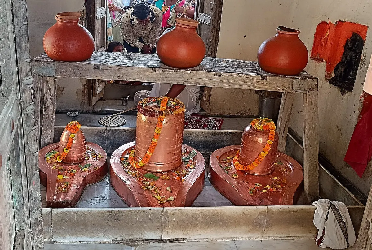 Three Shivlings garlanded with marigolds under dripping clay water pots